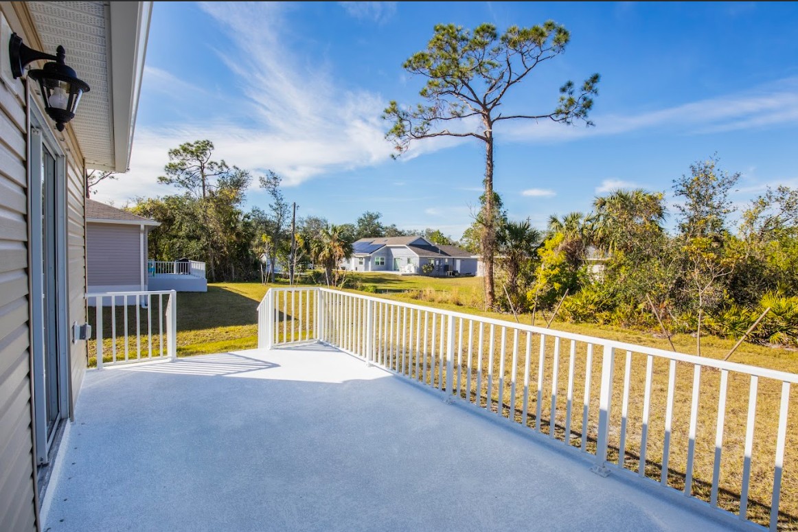 A sunny backyard view featuring a spacious deck with white railings and a lush green landscape in the background.