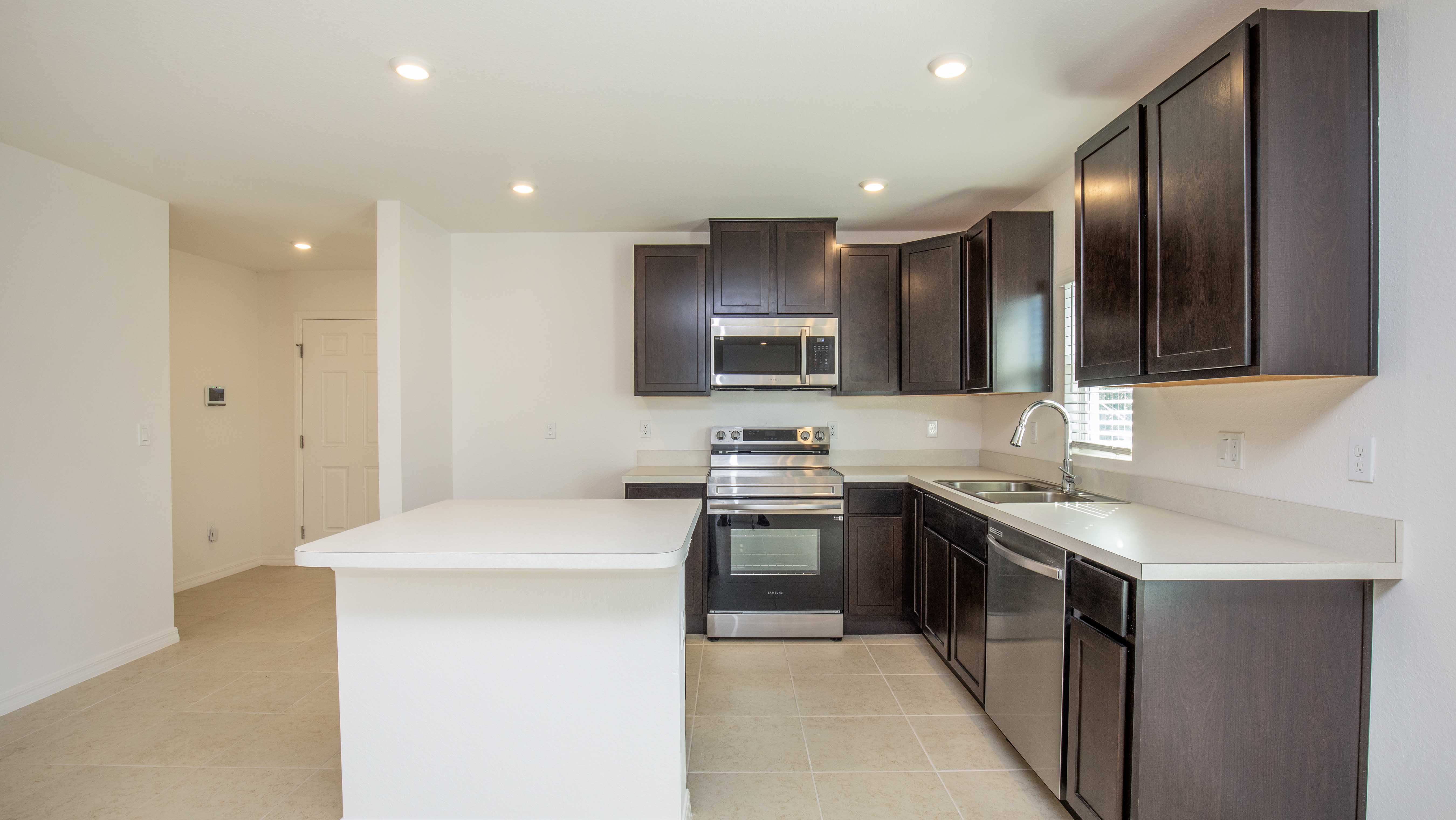 Modern kitchen with dark wood cabinetry, stainless steel appliances, and a light tile floor.