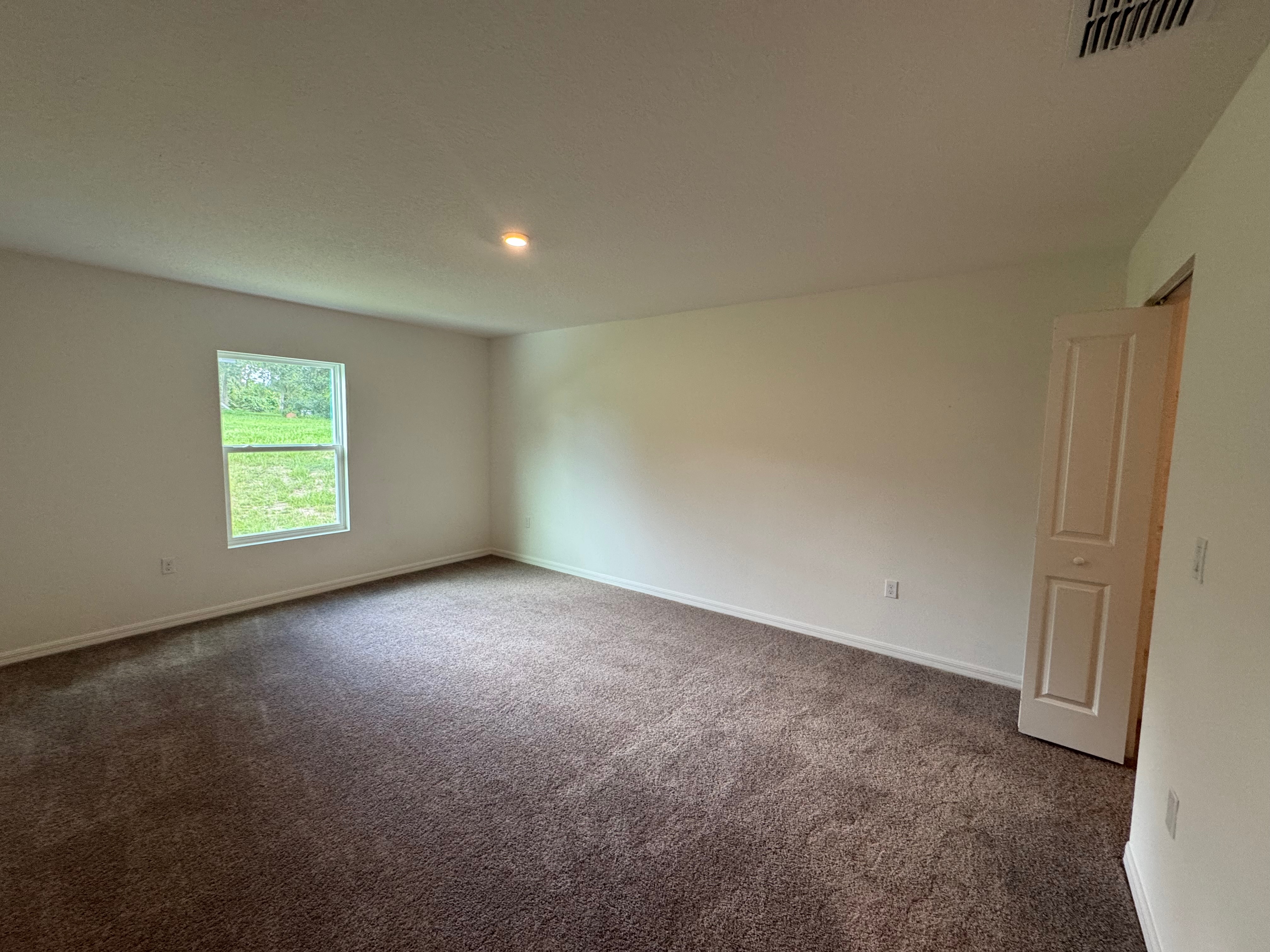 Spacious unfurnished room with beige carpeting, single window, and open closet door.