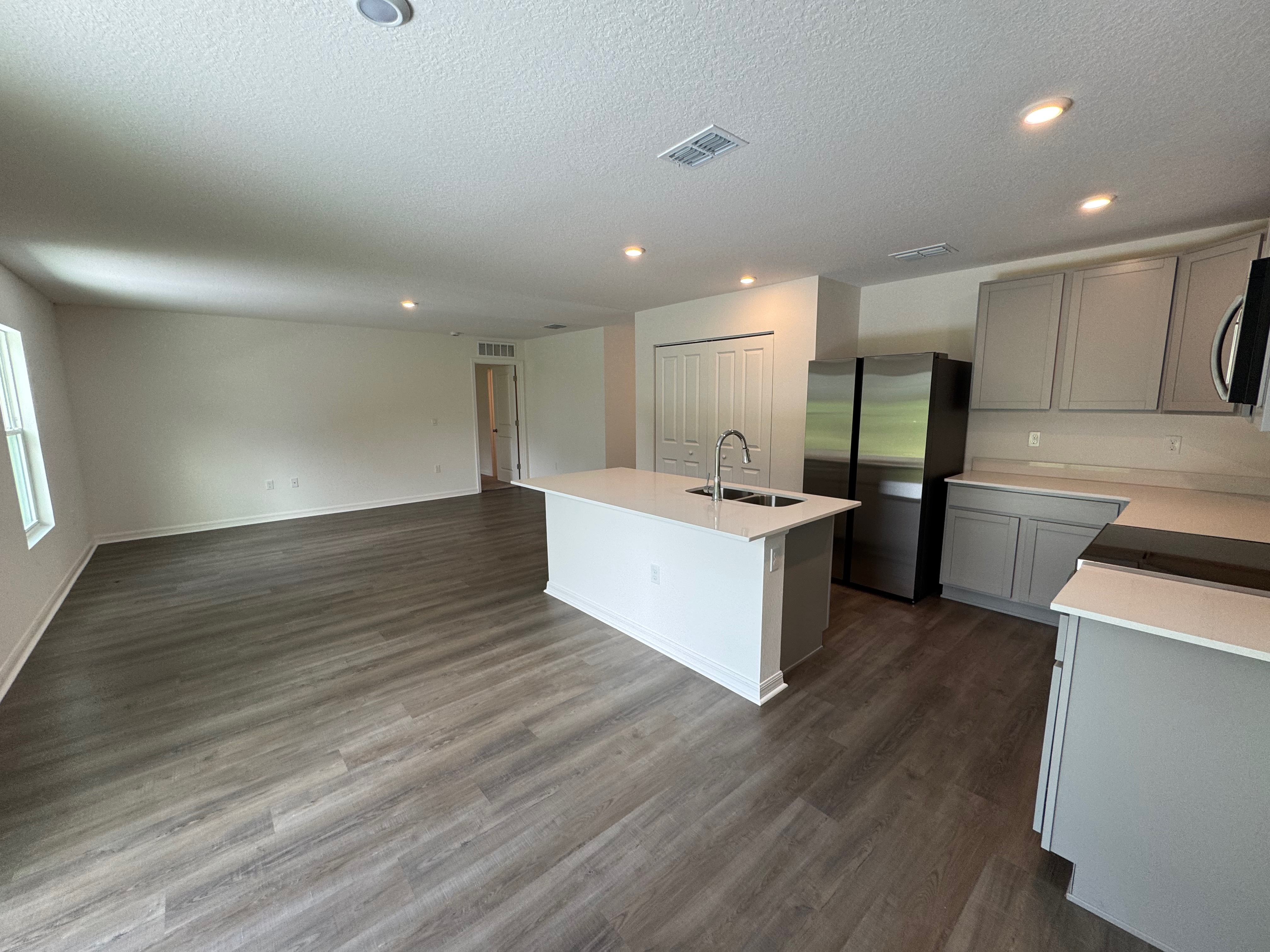 Modern open-concept kitchen and living area with hardwood flooring, island counter, gray cabinets, and recessed lighting.