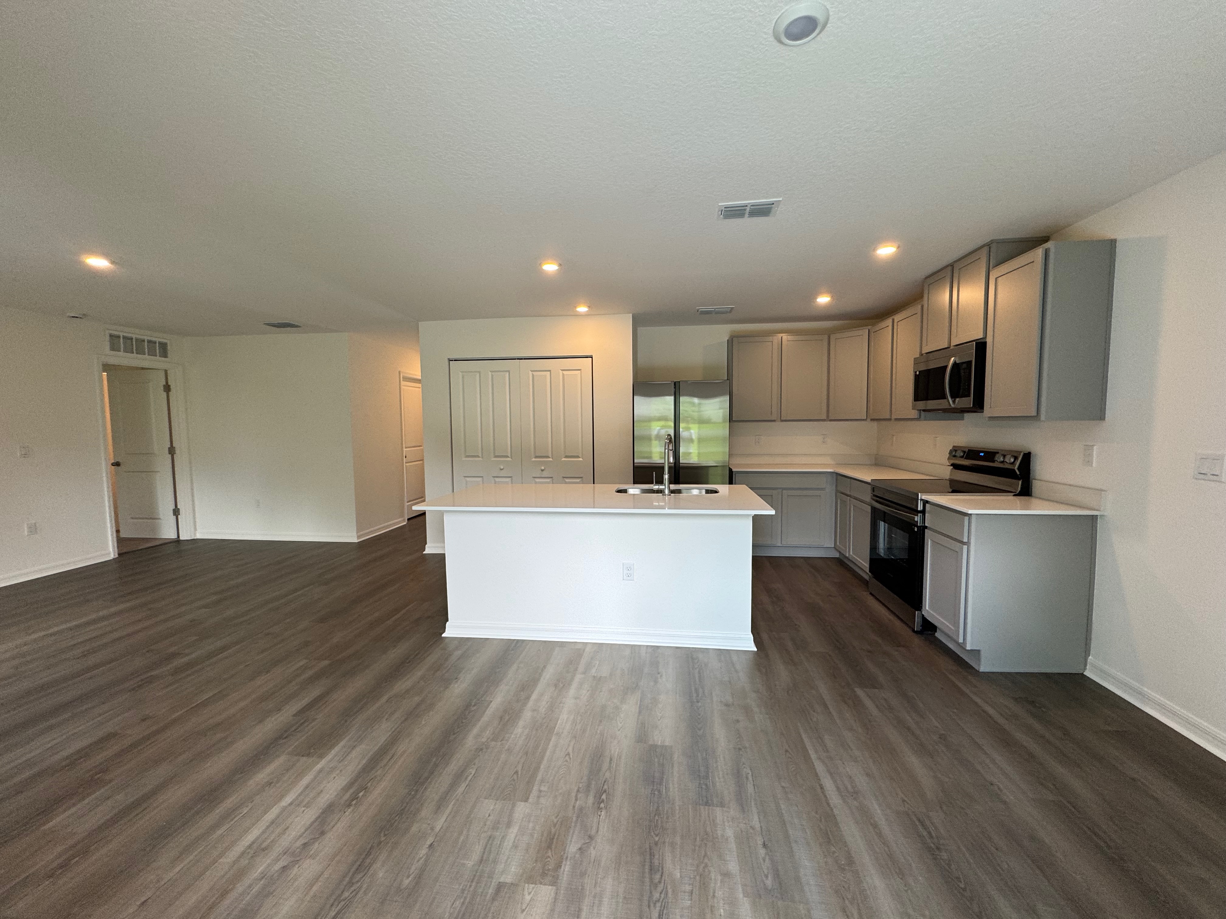 Modern kitchen and open living area in a new home with hardwood flooring and stainless steel appliances.