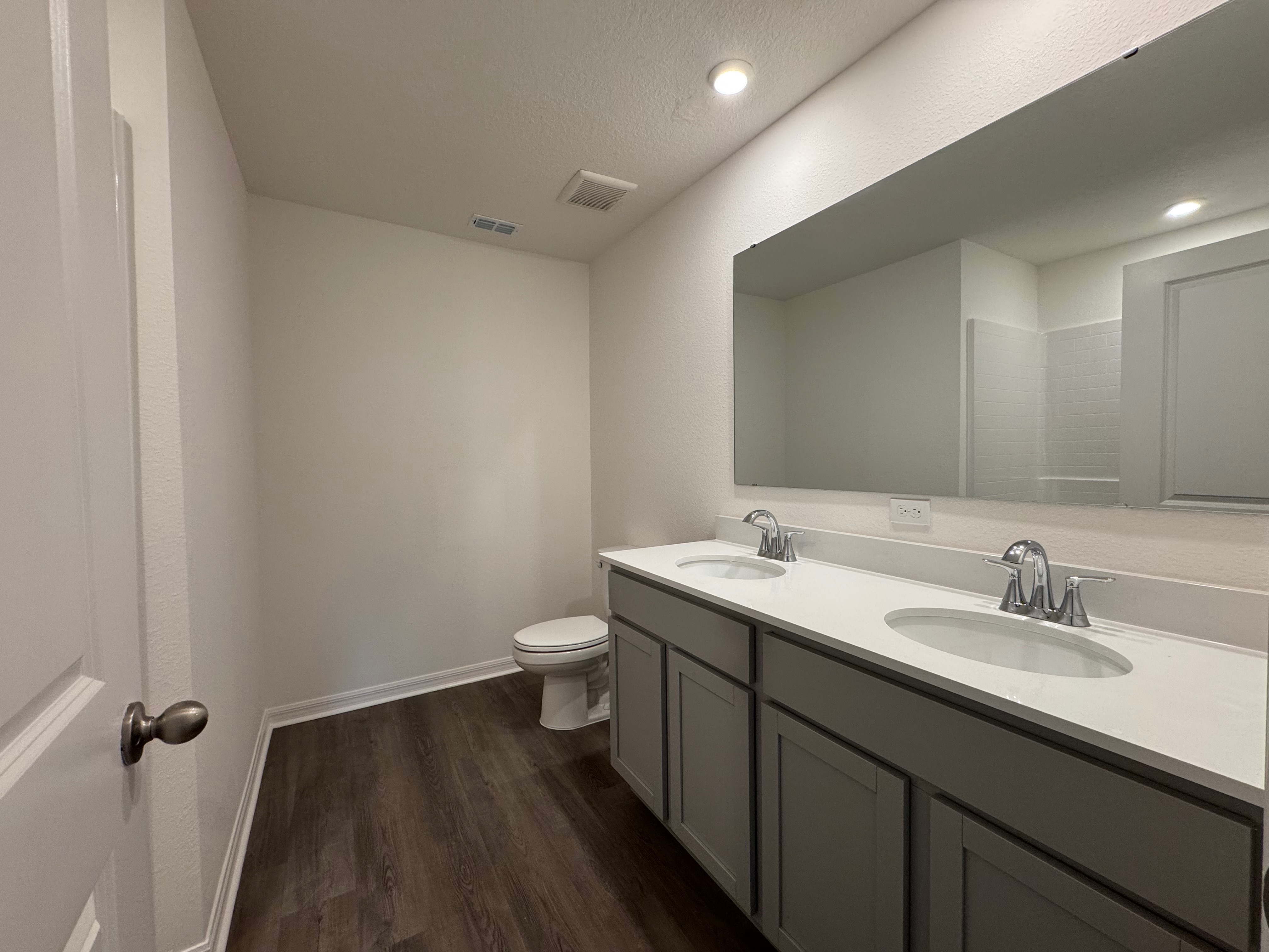 Modern bathroom with dual sinks, large mirror, dark wood flooring, and minimalist design.