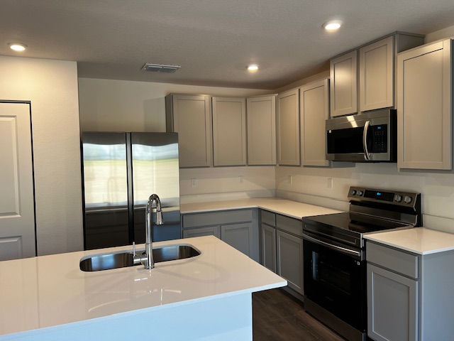 Modern kitchen with stainless steel appliances, light gray cabinets, and a white quartz countertop island.