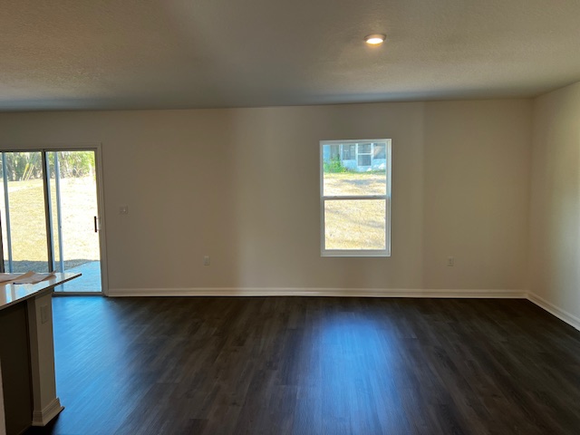 Spacious empty room with dark hardwood flooring, white walls, and natural light from sliding glass door and window.