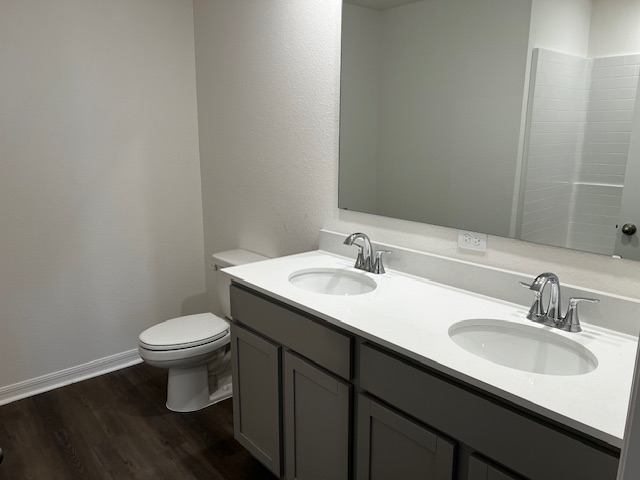 Modern bathroom with dual sinks, a large mirror, and a toilet, featuring a sleek design and dark wood flooring.