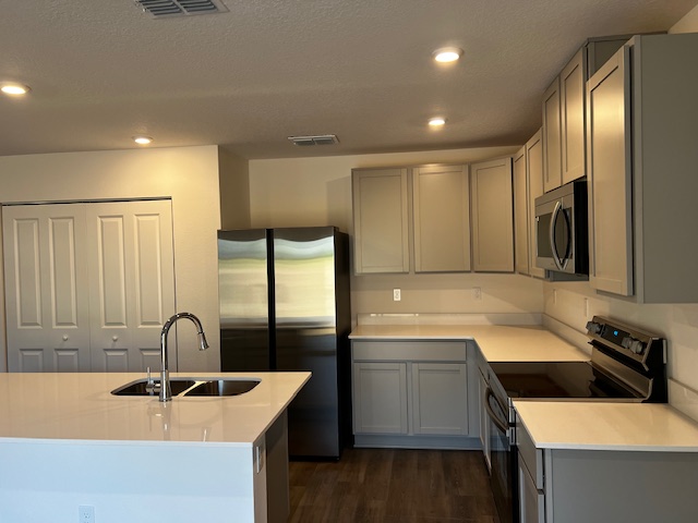 Modern kitchen with stainless steel appliances, beige cabinets, and recessed lighting.