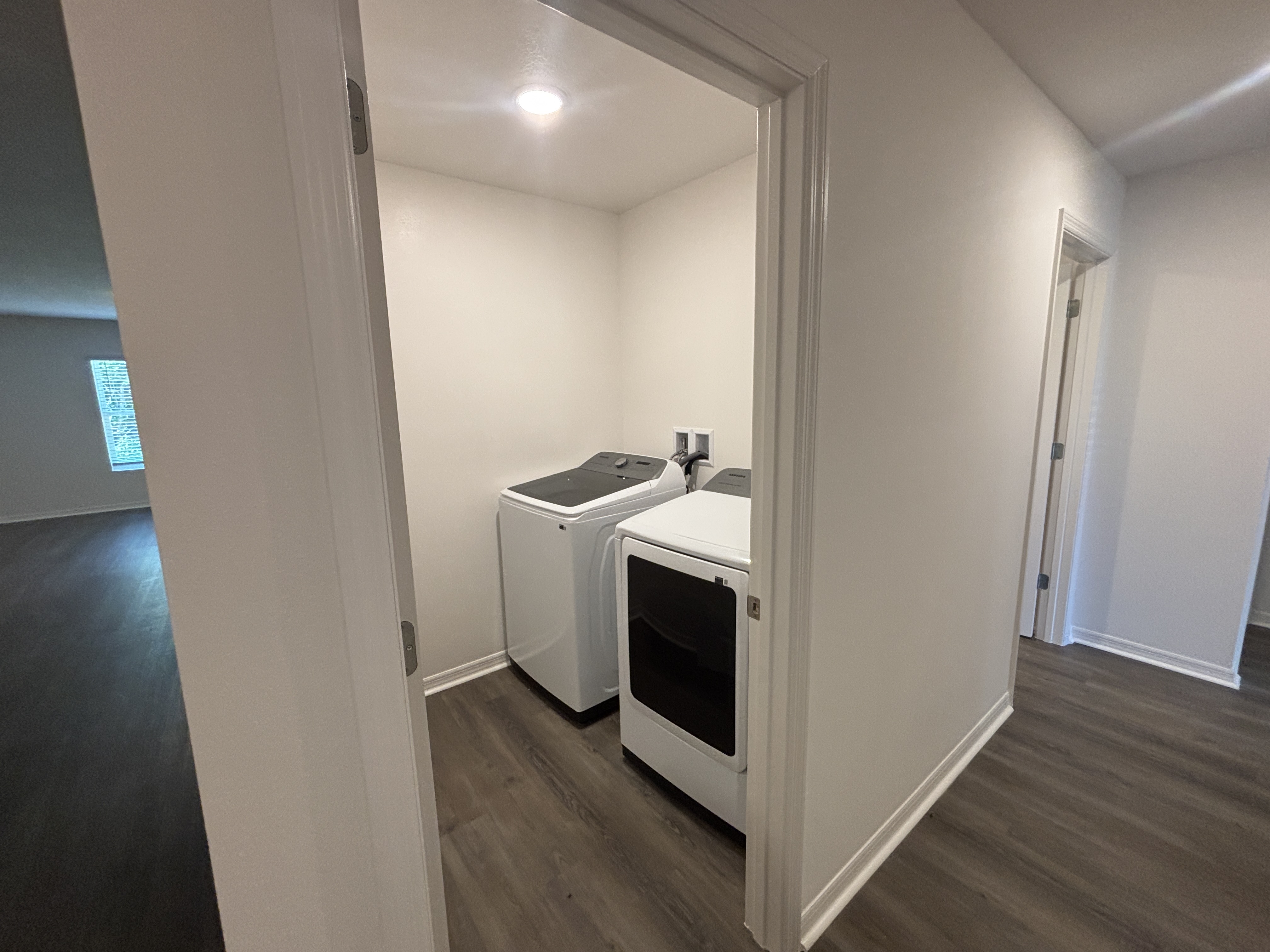 Modern laundry room with a washing machine and dryer on dark wood flooring.