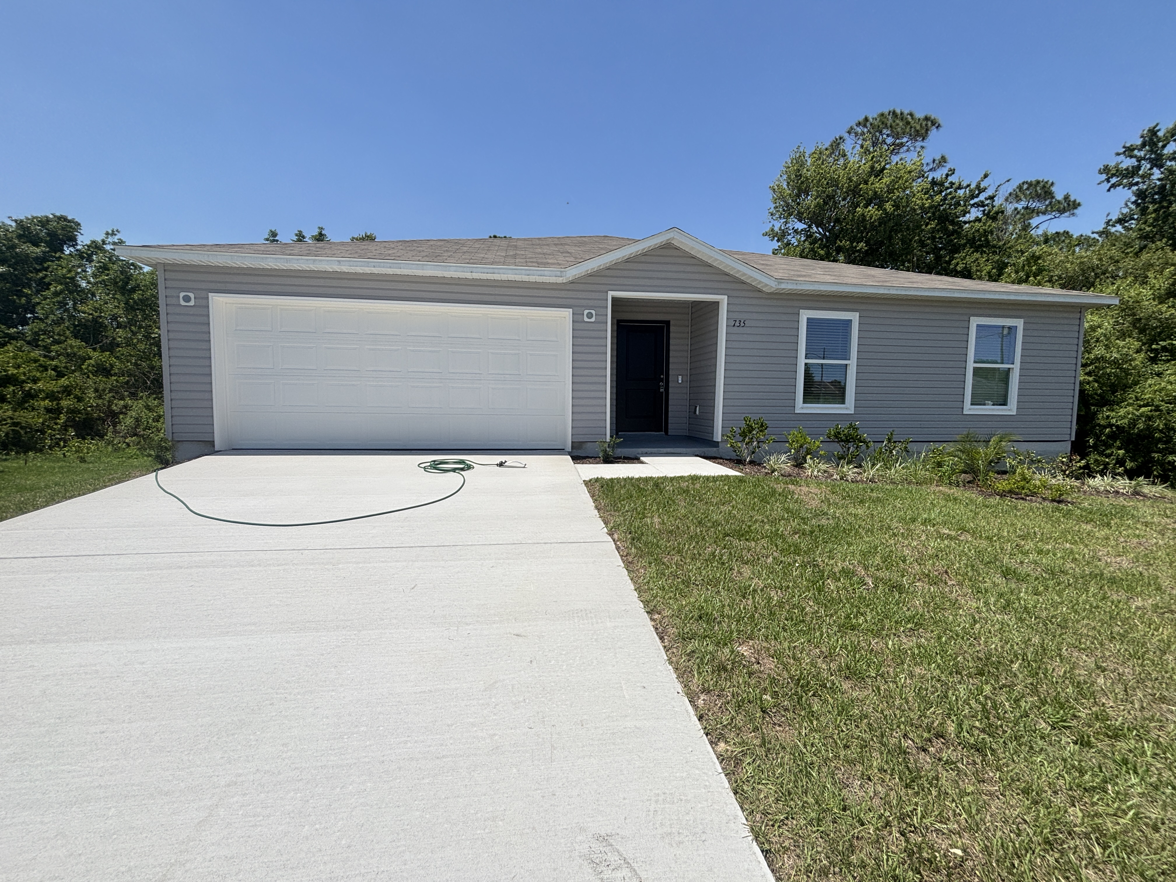 Newly-built single-story gray house with a two-car garage and a concrete driveway on a sunny day.
