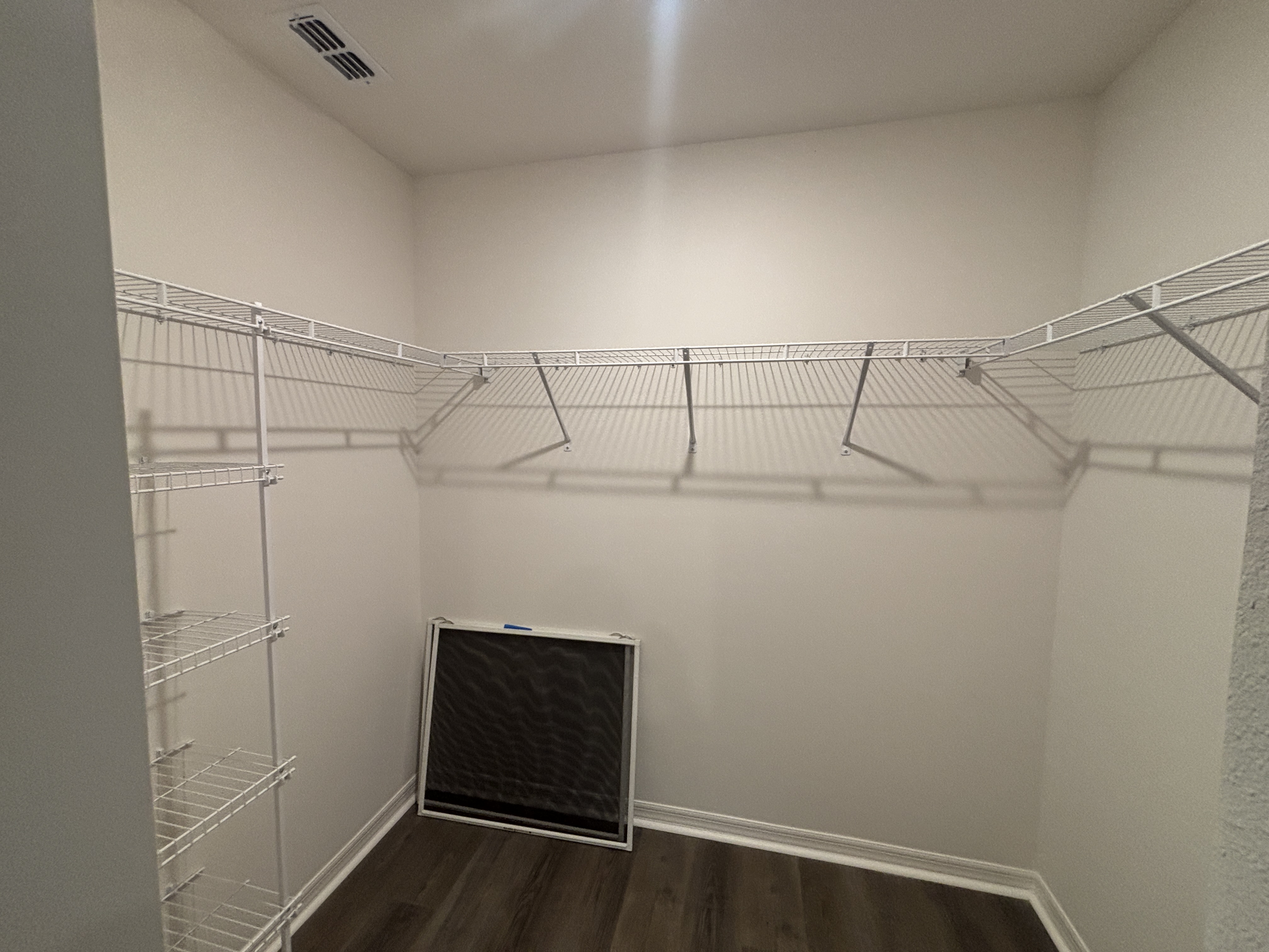 Empty walk-in closet with white wire shelving and hardwood floors.