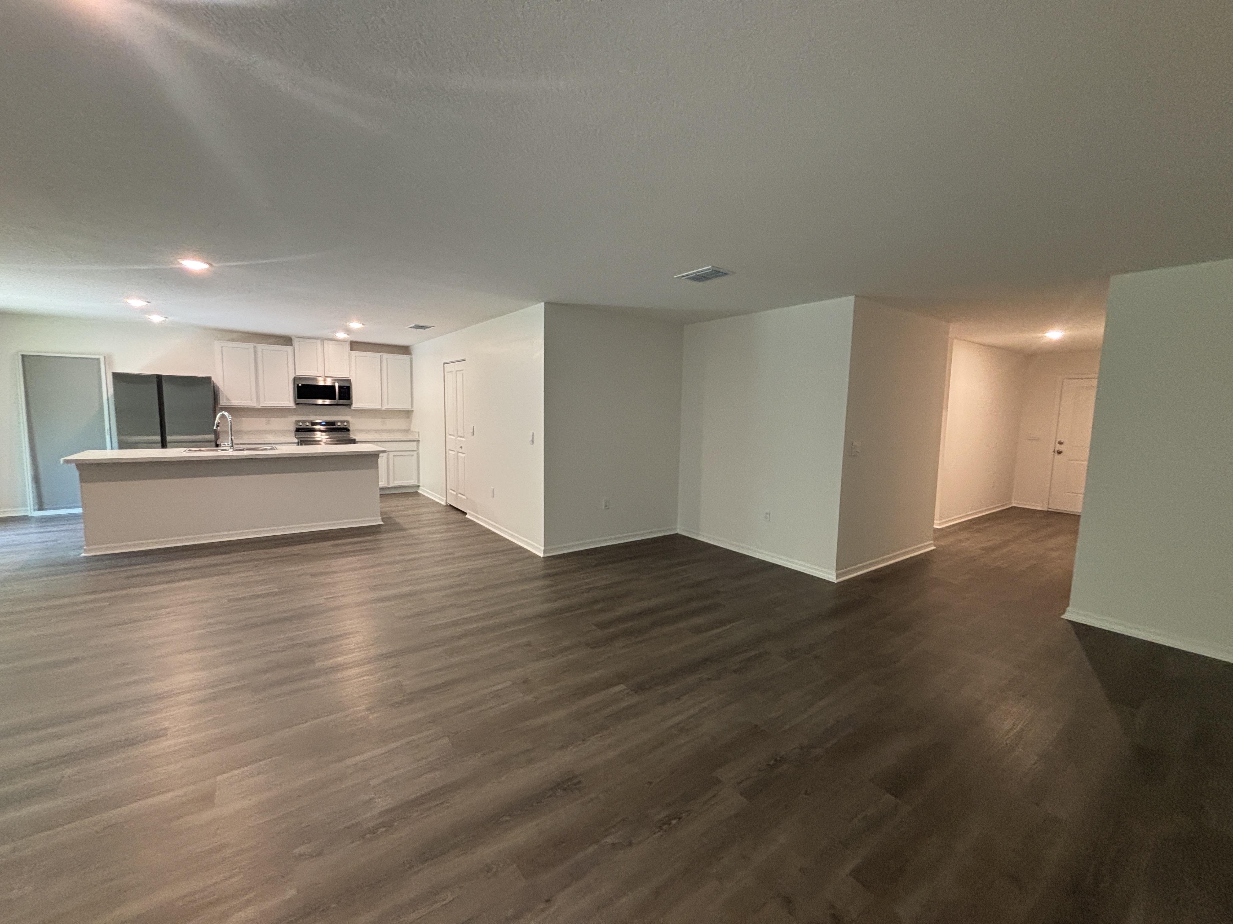 Spacious open-concept kitchen and living area with hardwood floors, white cabinets, and stainless steel appliances.