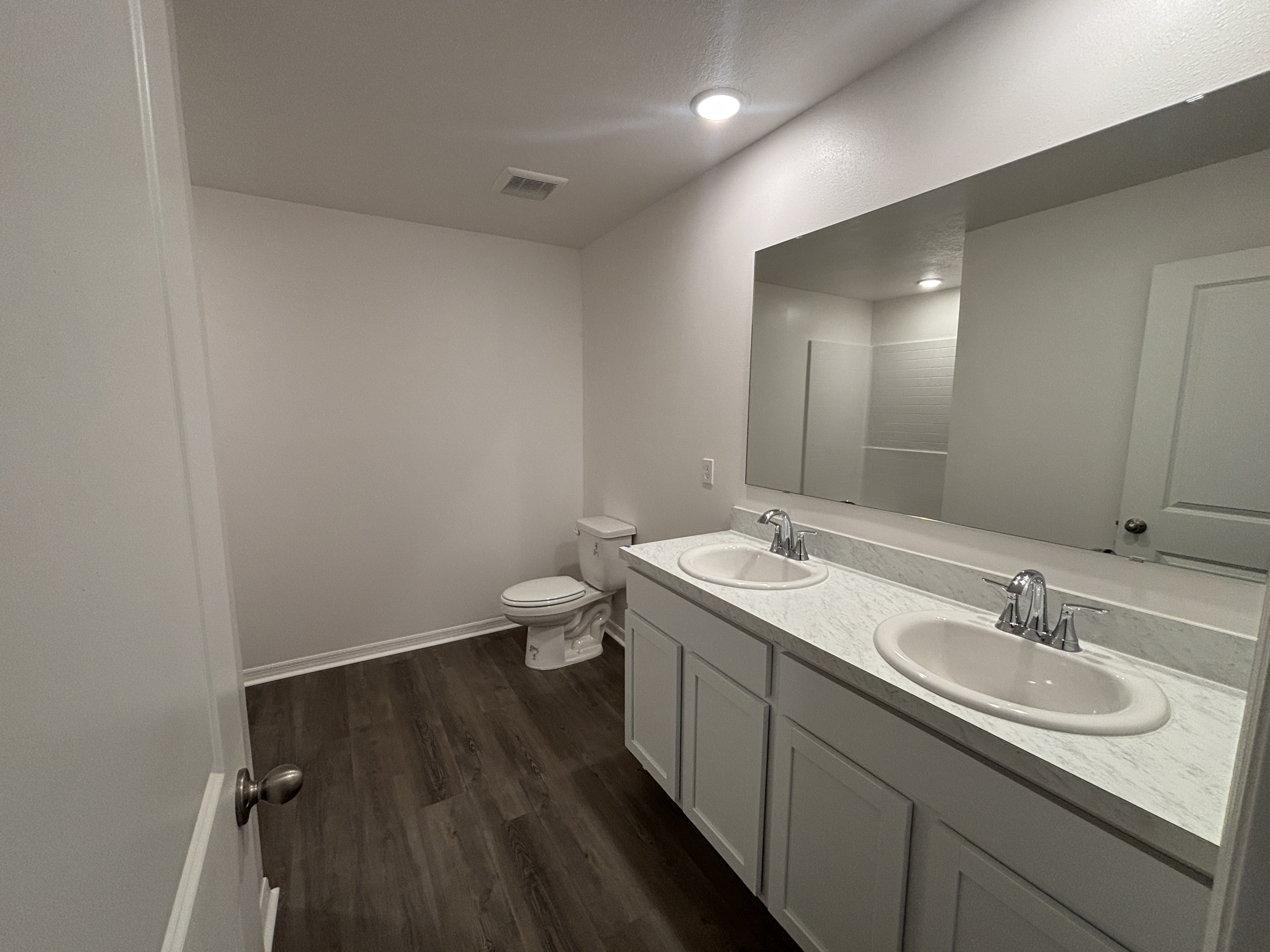 Modern bathroom with dual sinks, large mirror, and wooden floor.