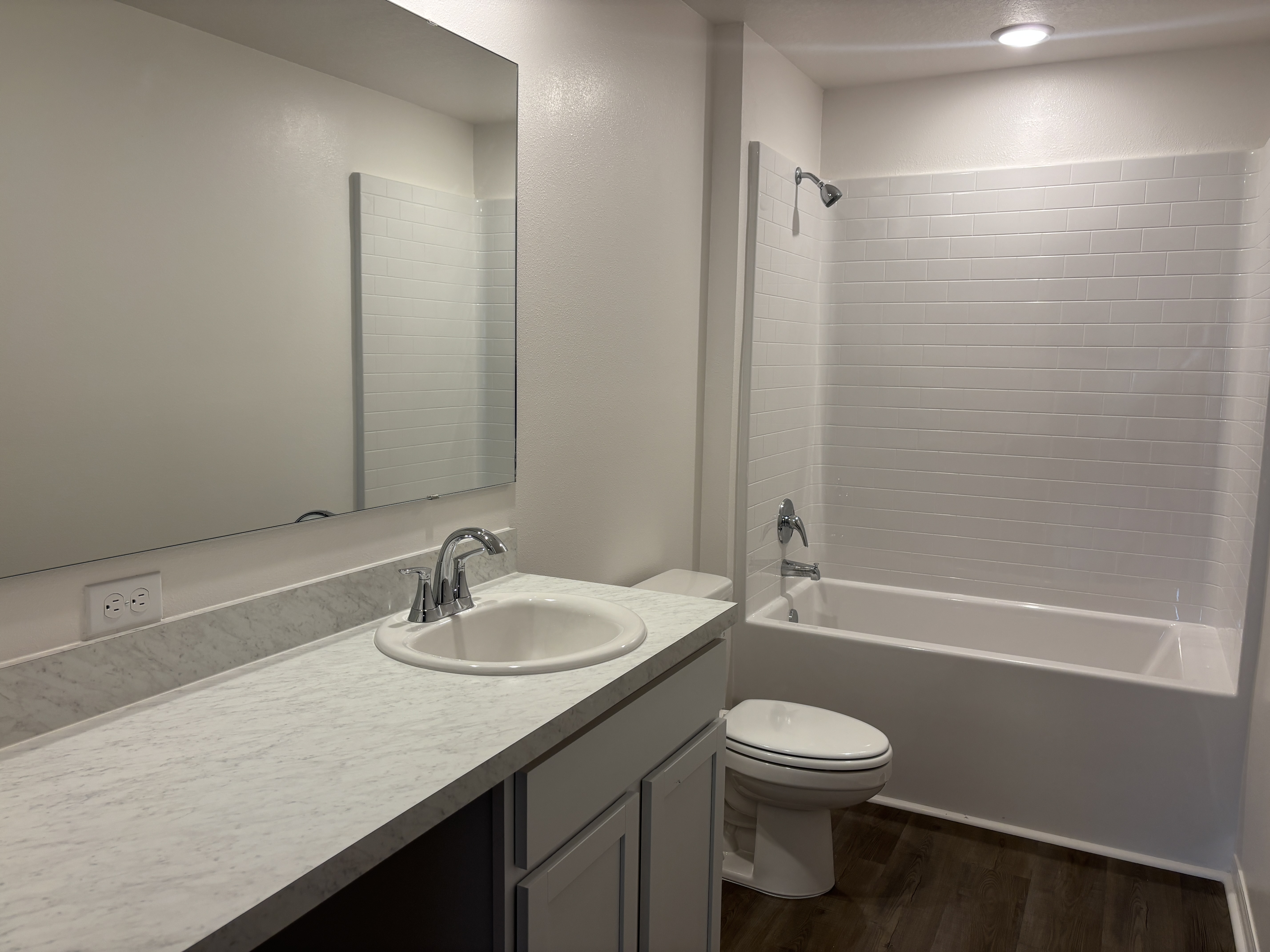 Modern bathroom with white tile bathtub, marble countertop, and wooden floor.