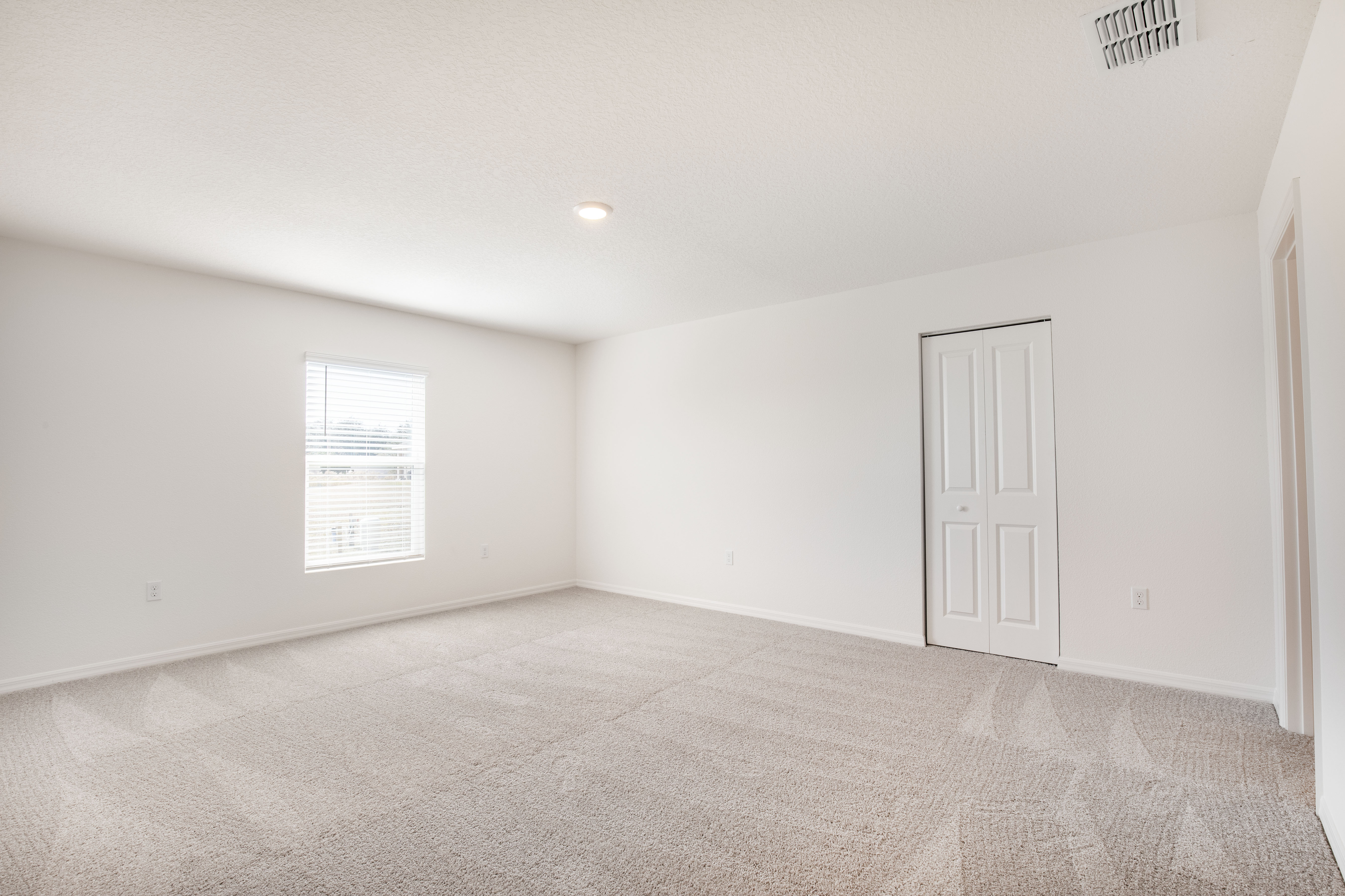 Empty carpeted room with white walls, a single window, and a closed door.