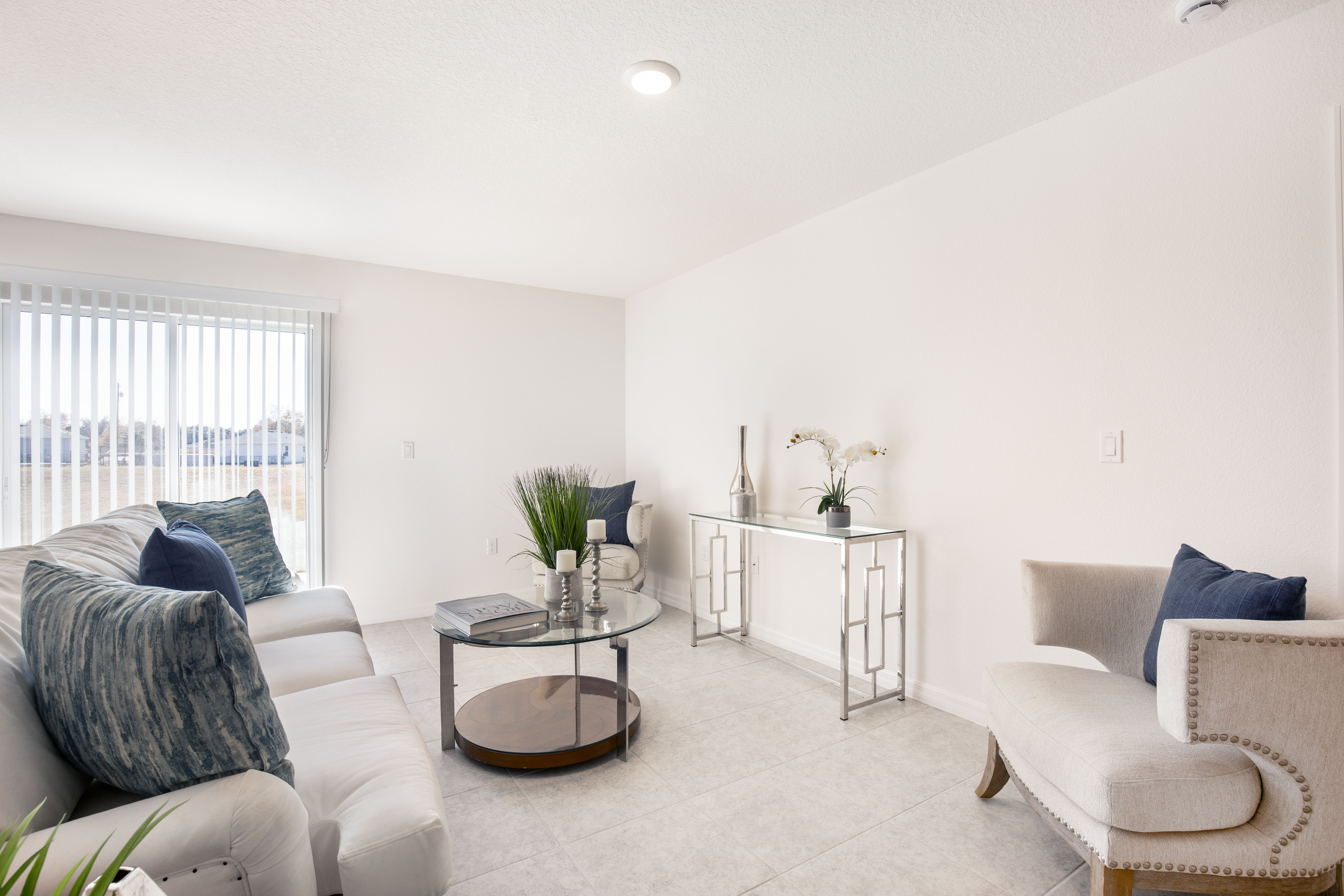 Modern living room with white walls, blue-accented sofa, glass coffee table, and decorative console table.
