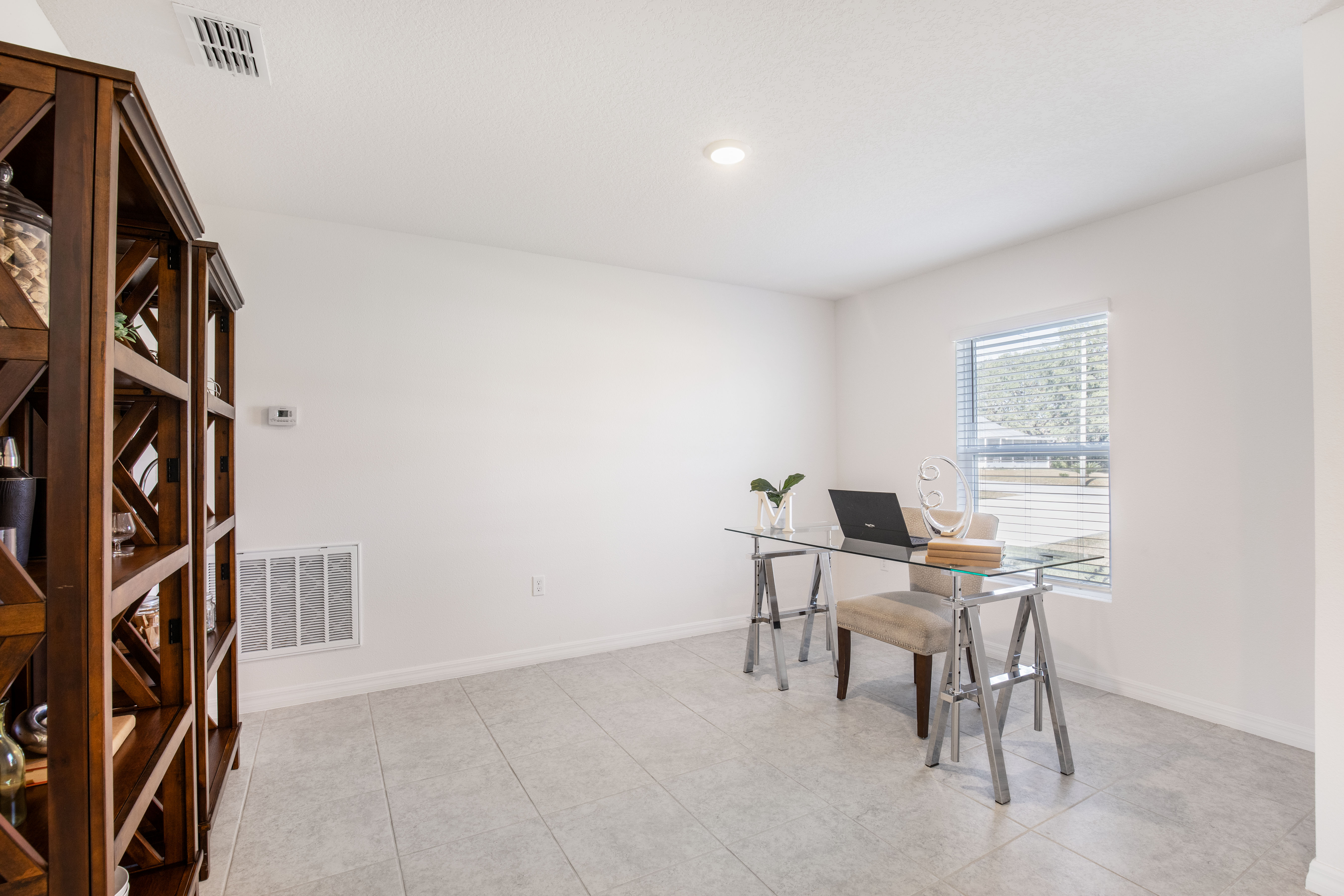 Minimalist home office with glass desk, laptop, and wooden shelves in a bright room.