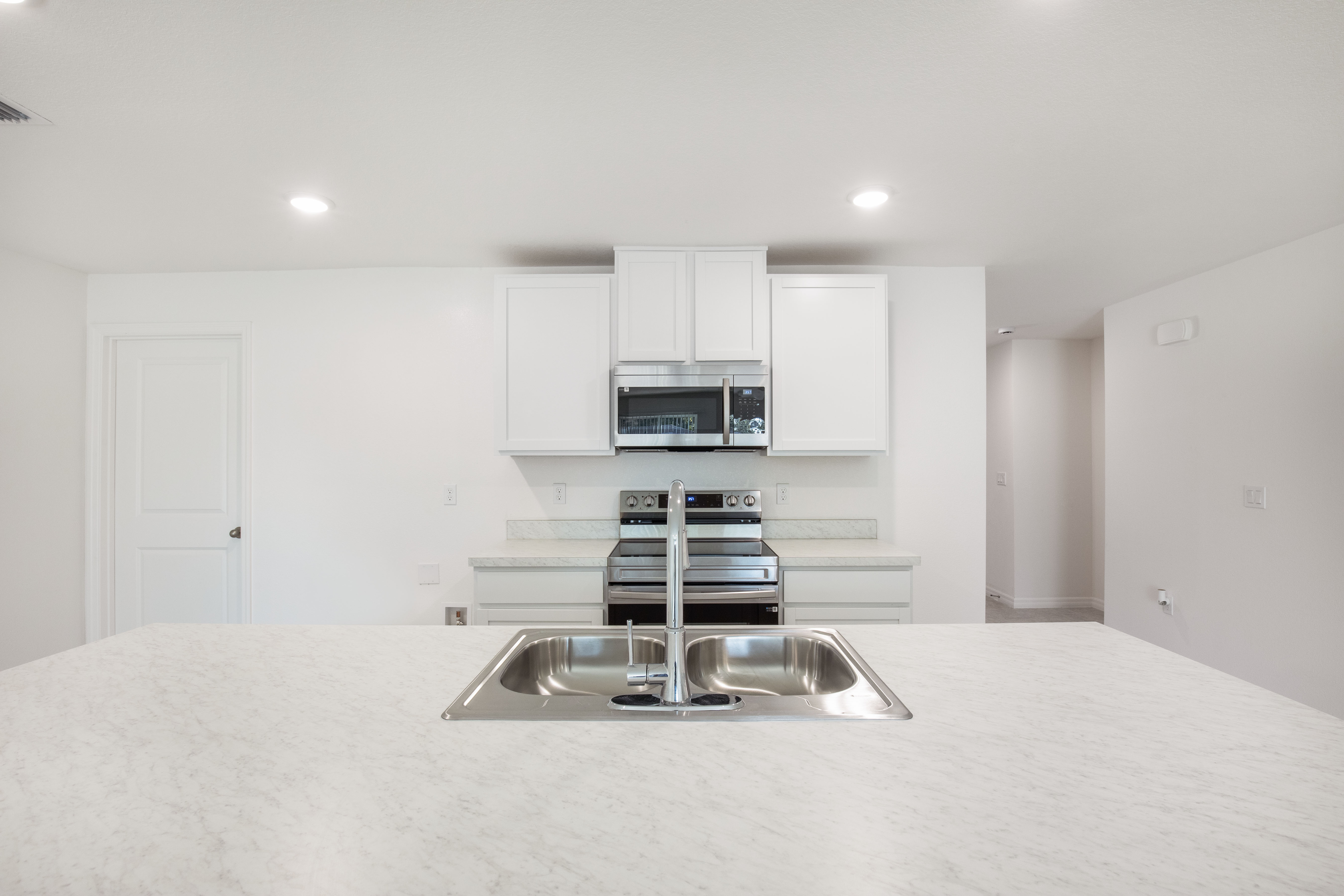 Modern kitchen with a stainless steel sink and faucet, white cabinetry, and built-in microwave over a sleek electric stove.